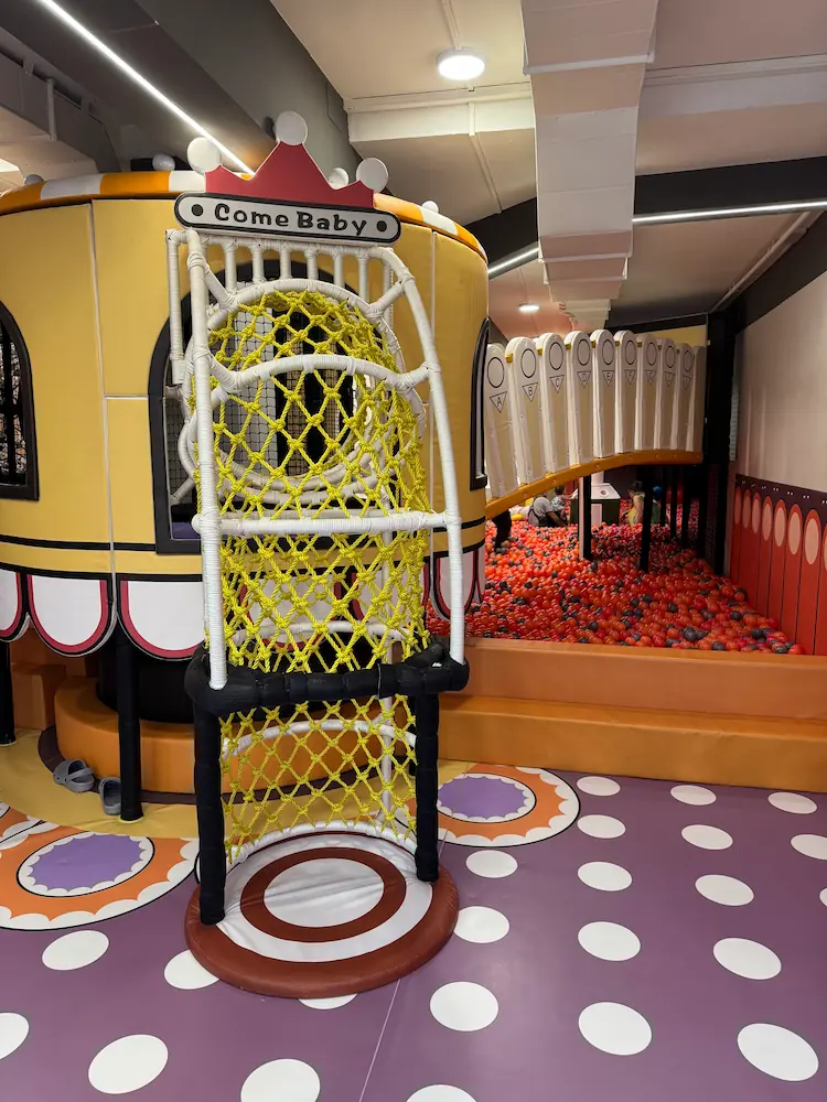 Zona de juegos infantil interior con piscina de pelotas, estructura con red para trepar y un túnel elevado decorado con colores vivos.