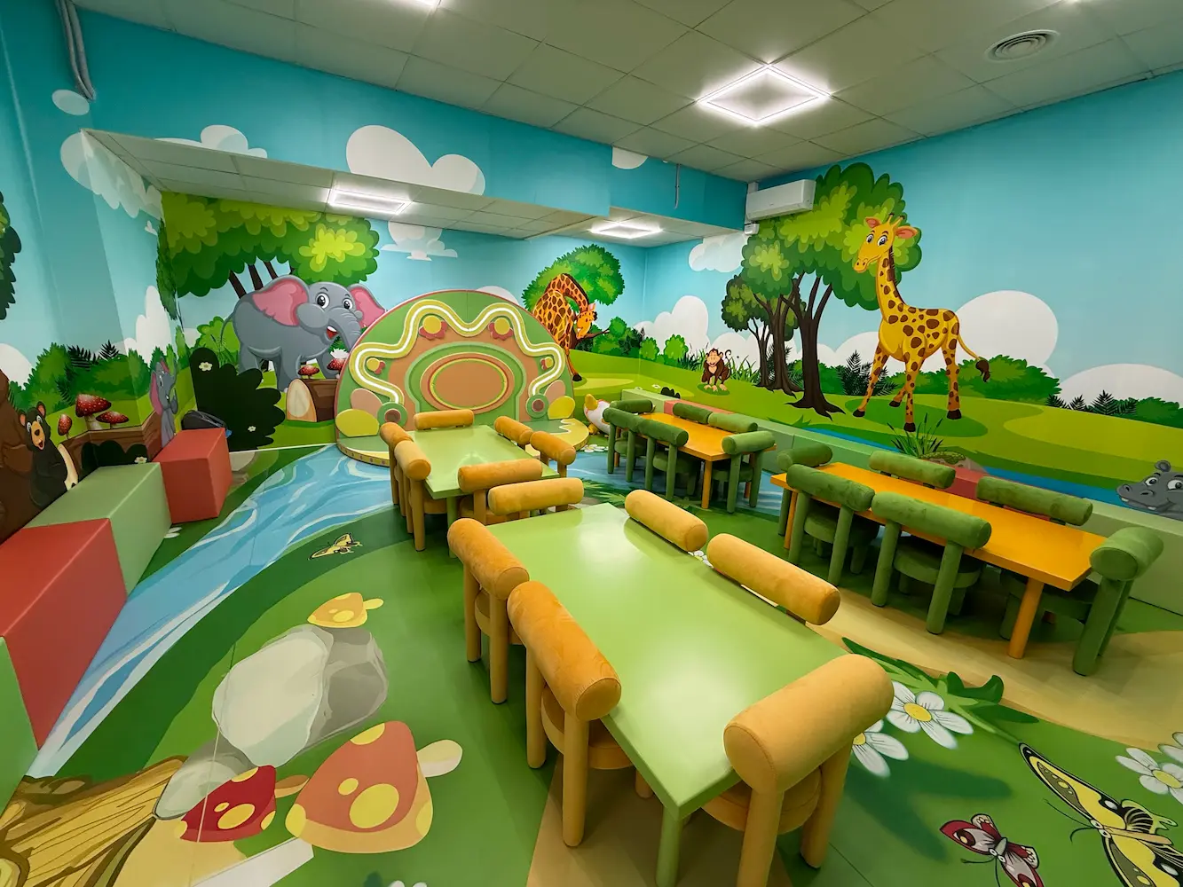 Sala infantil temática de la selva con animales y mesas de colores.
